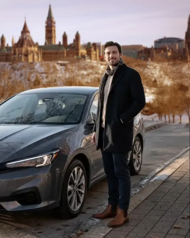A RideCan driver beside his sedan, with Parliament Hill across the river in winter